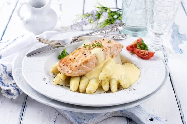 Asperges met zalm en hollandaisesaus op wit bord