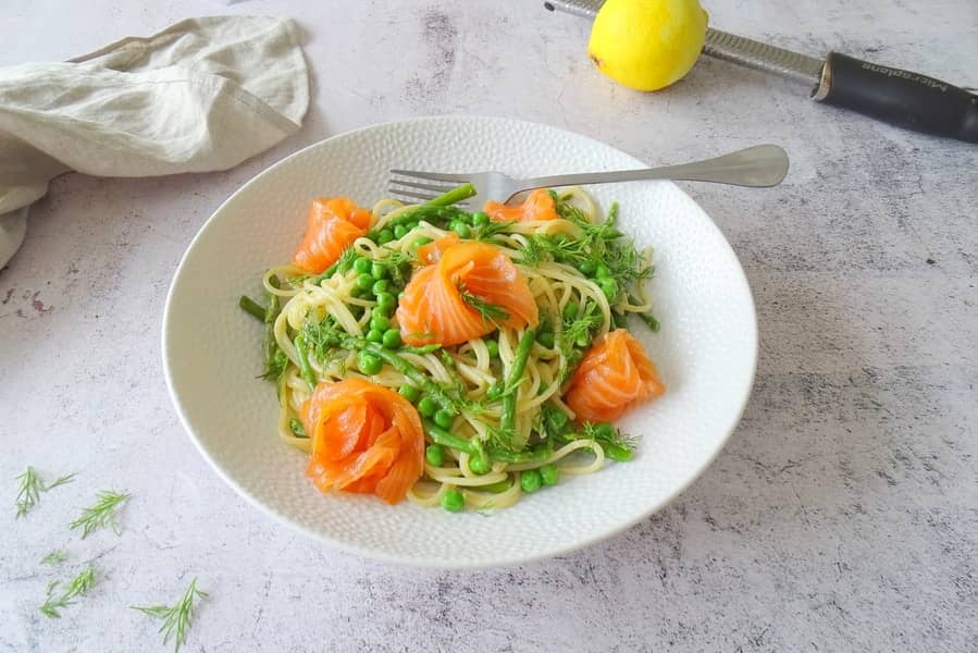 Spaghetti met zalm en asperge op wit bord en marmer blad