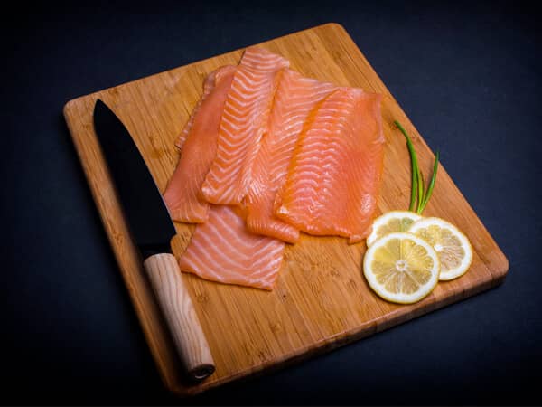 Koud gerookte zalm met traditioneel mes en serveerplank op zwarte achtergrond