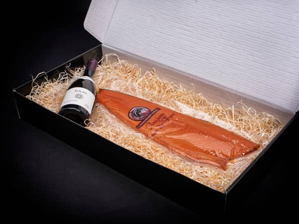 Geopende geschenk doos met zalm en fles wijn liggend in stro