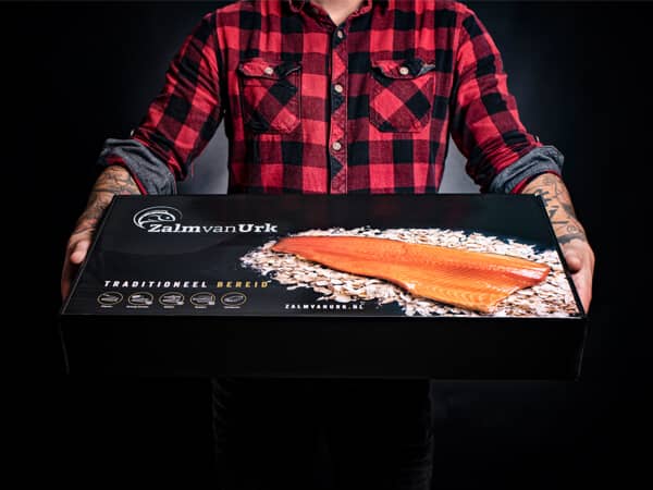 Geschenkdoos met gerookte zalm vastgehouden door man met tattoo