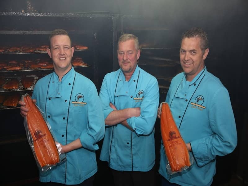 De jongens van de fant poseren met gerookte zalmen voor een rookoven