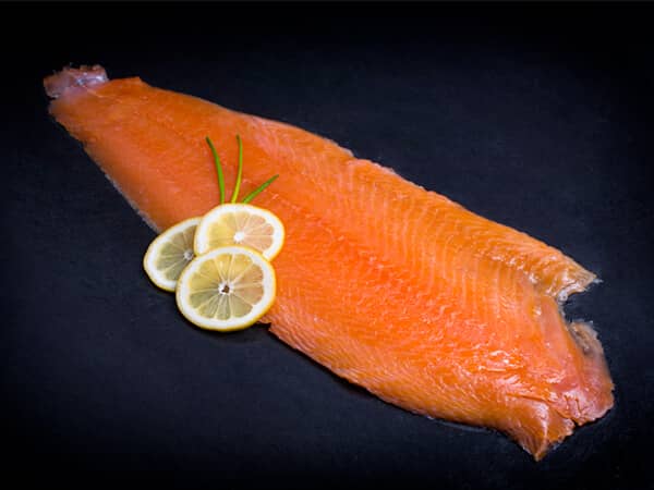 Koud gerookte zalm getrancheerd met schijfje citroen op zwarte achtergrond
