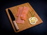 Koud gerookte zalm plakjes met mes en snijplank op een zwarte achtergrond