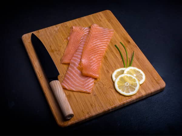 Koud gerookte zalm plakjes met mes en snijplank op een zwarte achtergrond